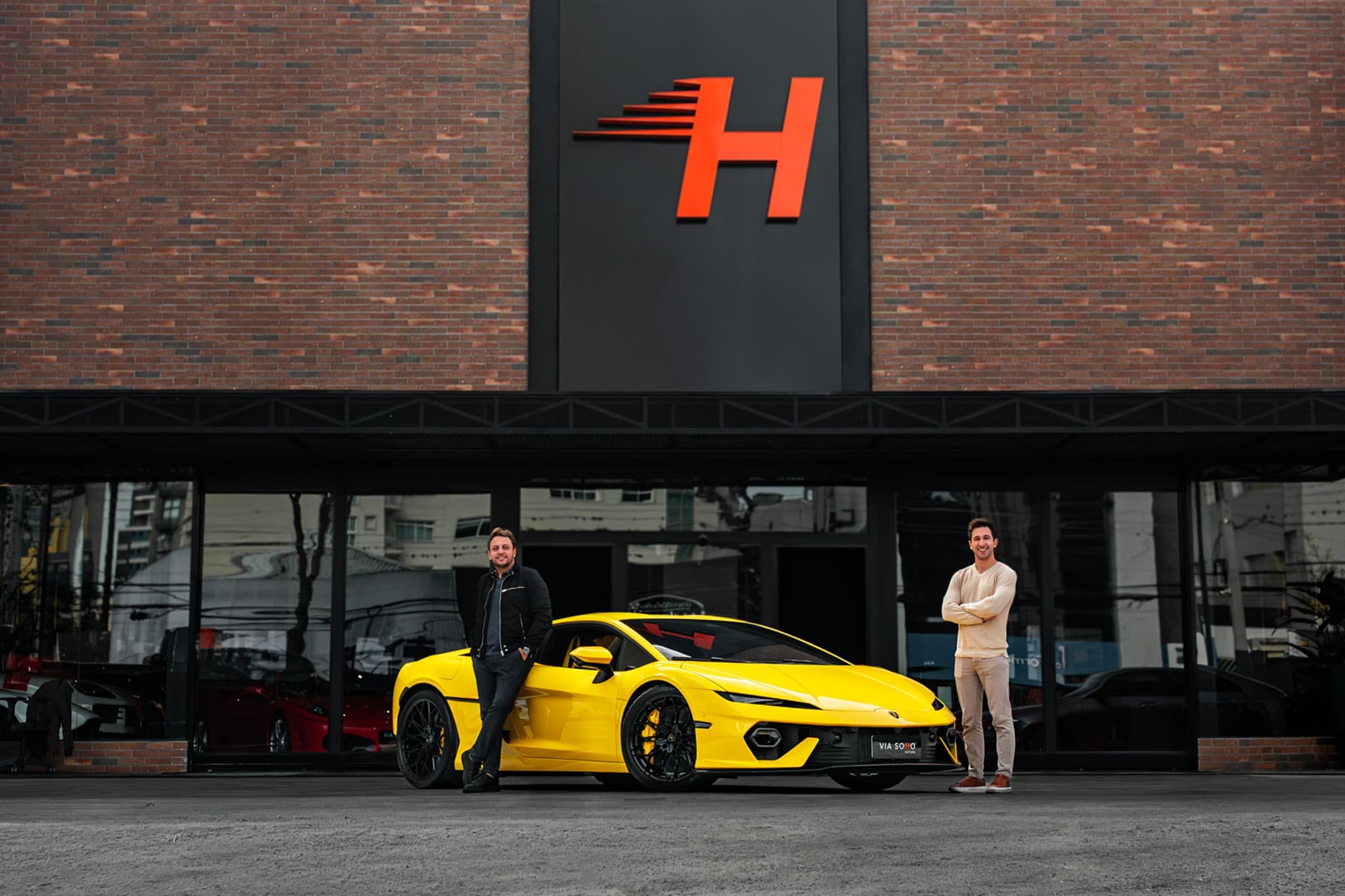 Diretores da Via Soho Motors em frente ao showroom com uma Lamborghini amarela